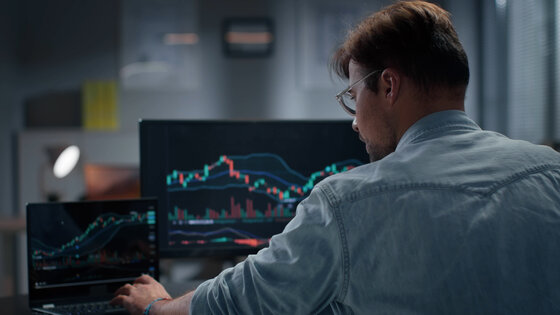 Rear view of trader working with stock market on laptop late in offic
