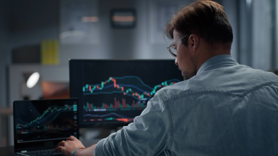 Rear view of trader working with stock market on laptop late in offic