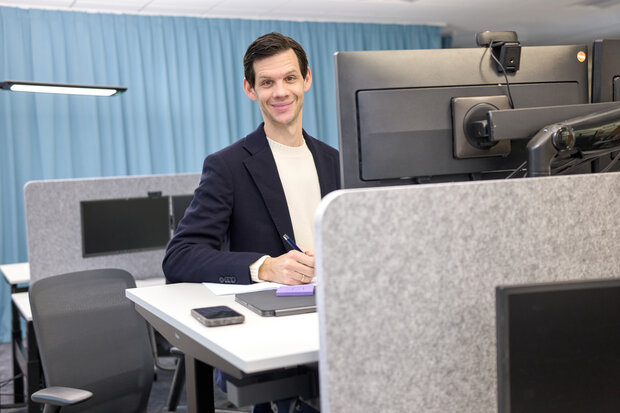 0034_Einzelperson_am_Schreibtisch_RolandBreitschuh Mann im dunkelblauen Jackett arbeitet am Schreibtisch und schaut in die Kamera, Querformat